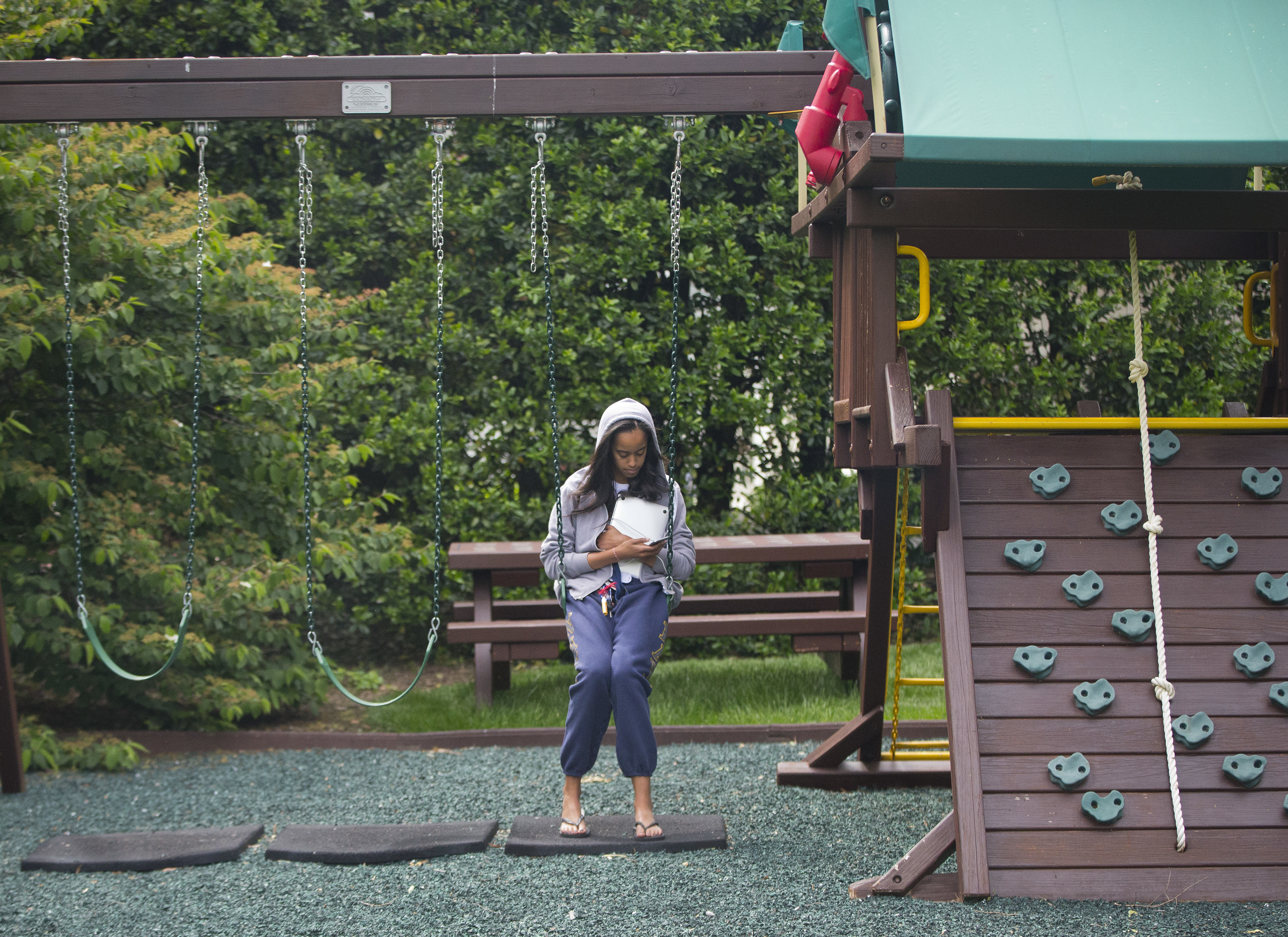 FILE - In this May 18, 2016 file photo, Malia Obama uses her phone at the swing and play set on the south grounds of the White House outside of the Oval Office in Washington. The swing set that President Barack Obama installed on the South Lawn for his young daughters eight years ago has a new home. The White House says the Obamas donated the set to a shelter in southeast Washington. The Obamas are planning to visit the Jobs Have Priority Naylor Road Program and join residents for a service project Monday in honor of Martin Luther King Jr. Day. (AP Photo/Pablo Martinez Monsivais, File)