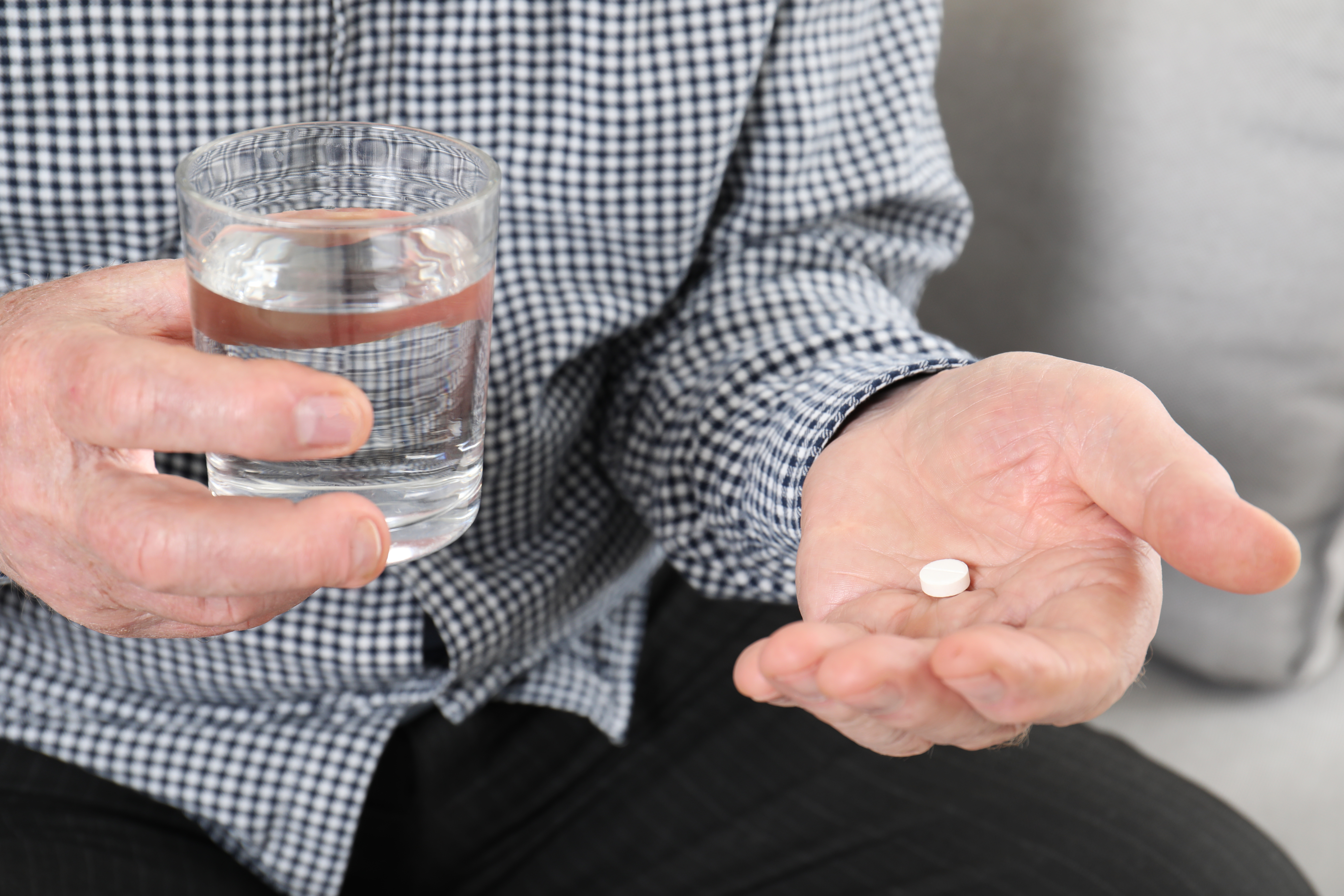 Senior man holding pill and glass of water, closeup